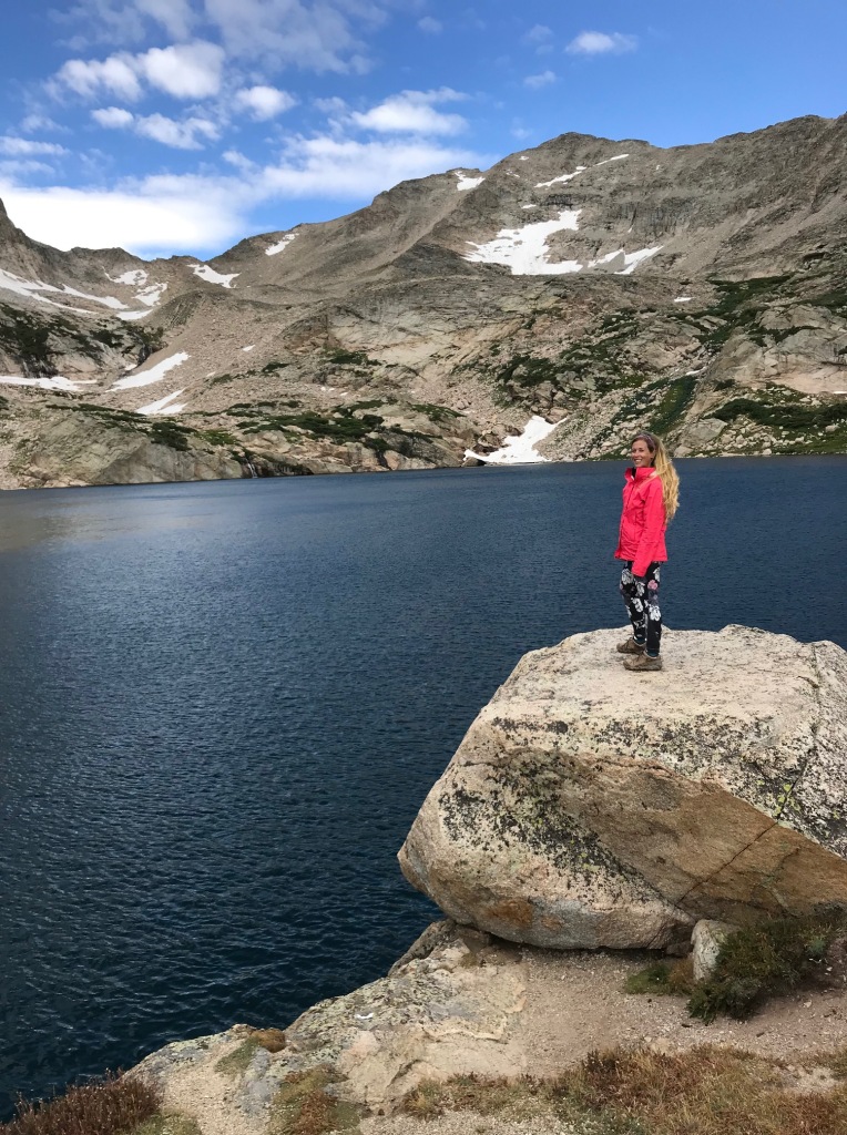 Woman stands in front of Blue Lake in the Brainard Lake Recreation Area in the Indian Peaks Wilderness in Colorado. 